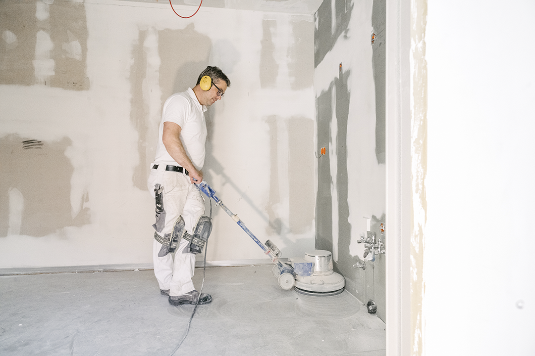 Ein Mitarbeiter von Malzeit schleift den Boden mit einer Maschine ab