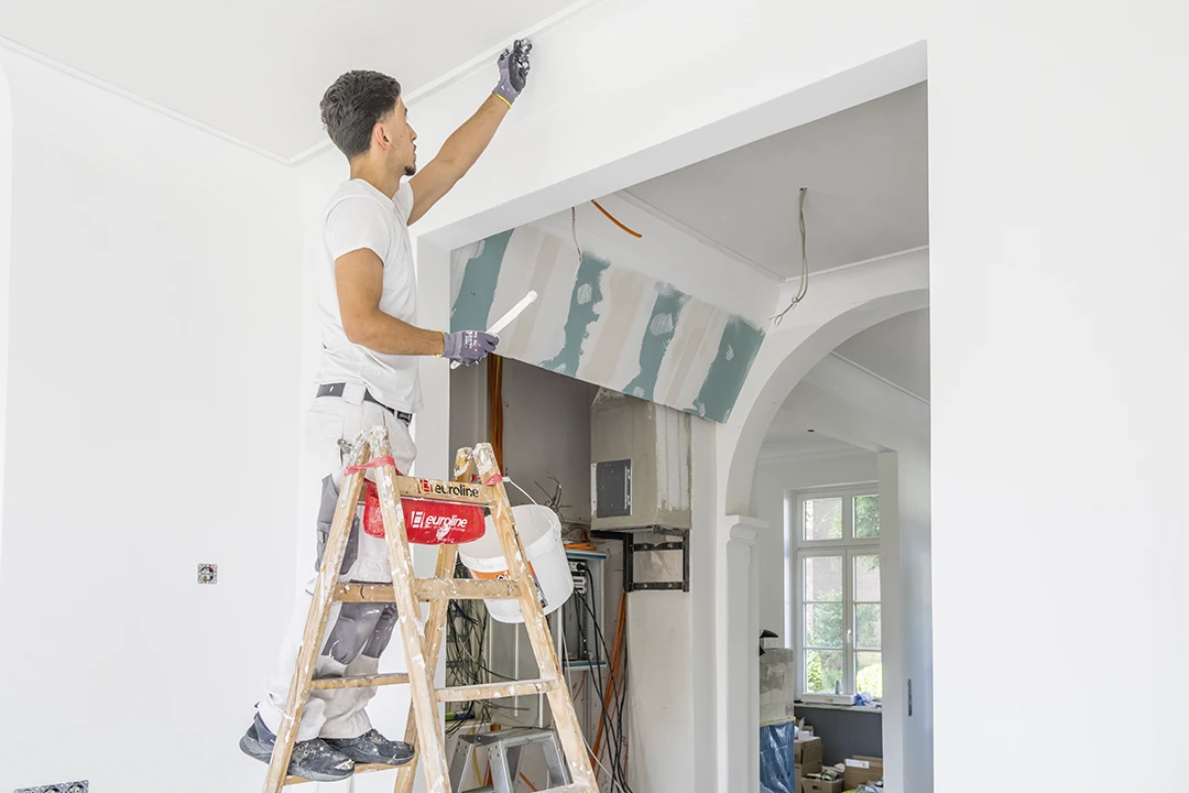 Ein Maler malt die Leisten der Decke sauber an